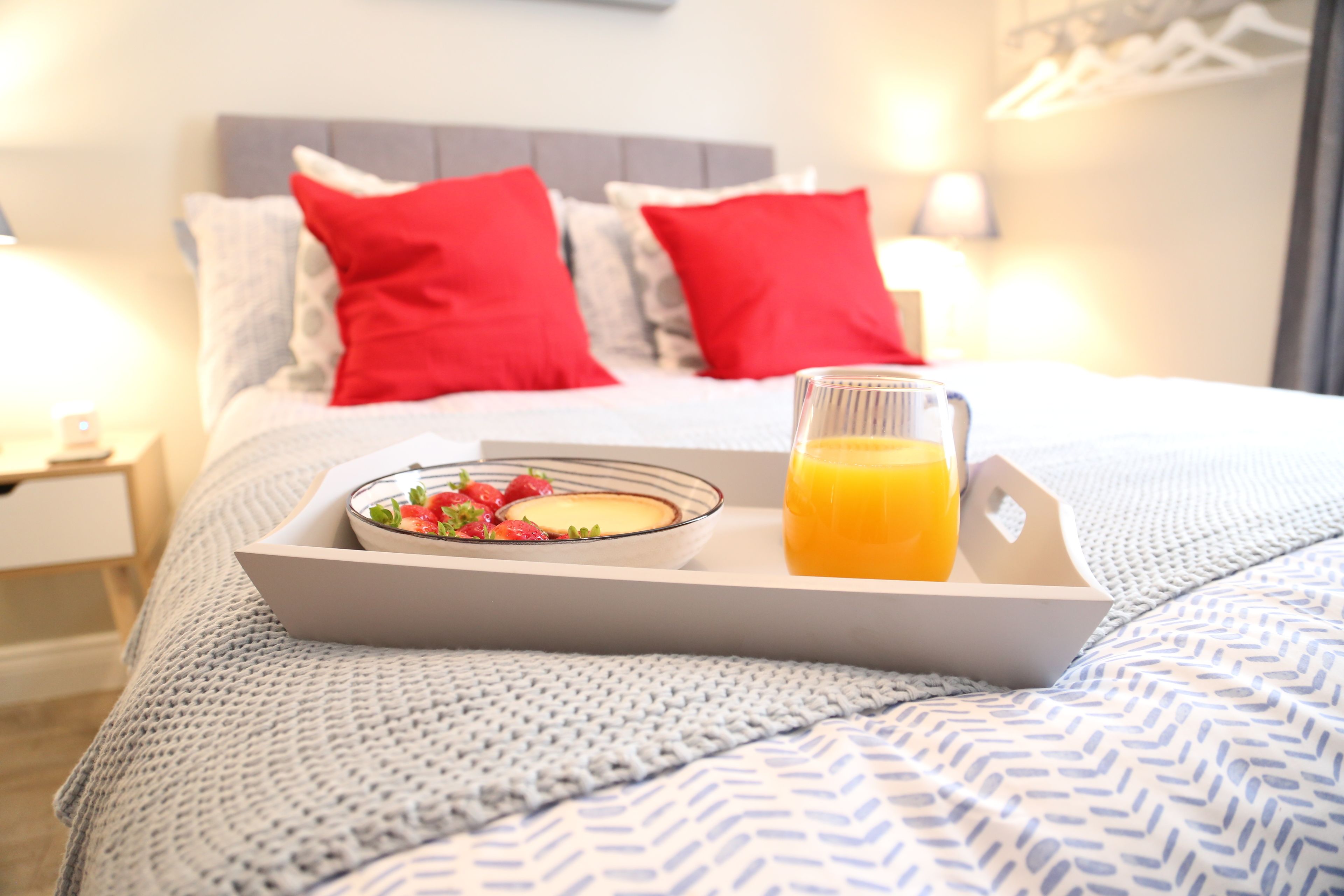 Una bandeja de desayuno ordenada sobre una cama, con un tazón de cereal y un vaso de jugo de naranja.