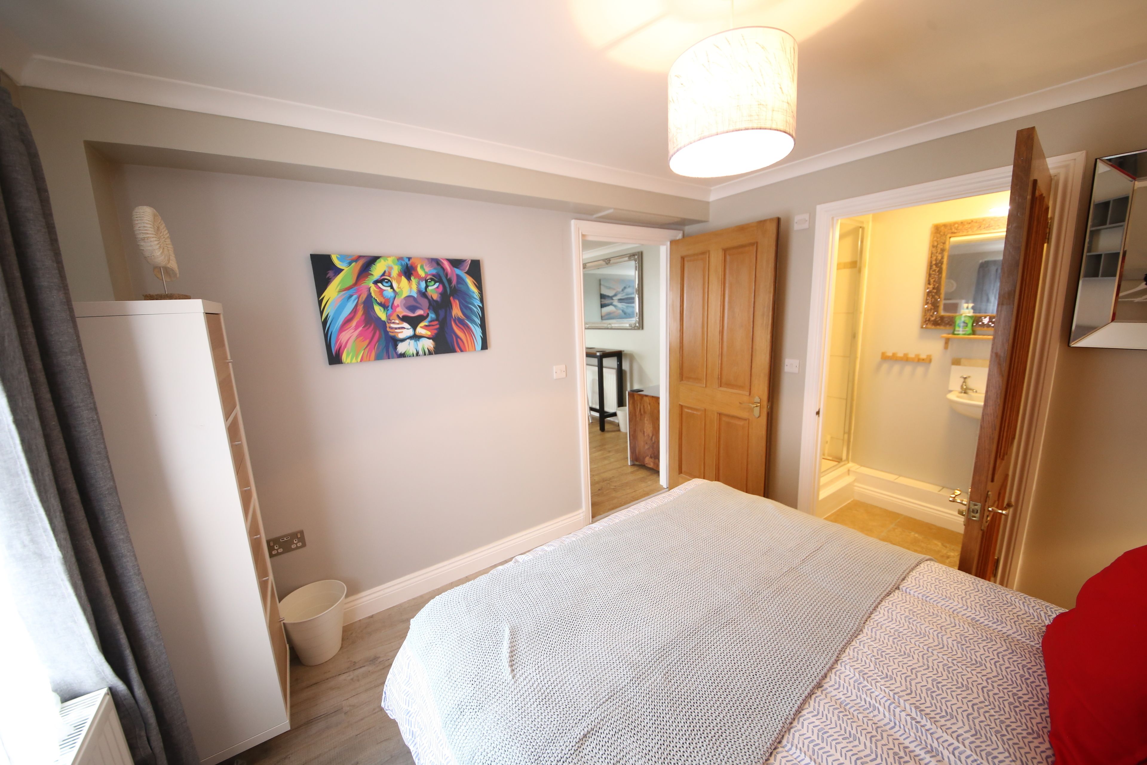 A bedroom with a bed, a wardrobe, a painting, and a bathroom visible through an open door.