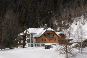 A multi-story building with a snow-covered roof, surrounded by a forested area. - Gasthof Tetter (Schladming)