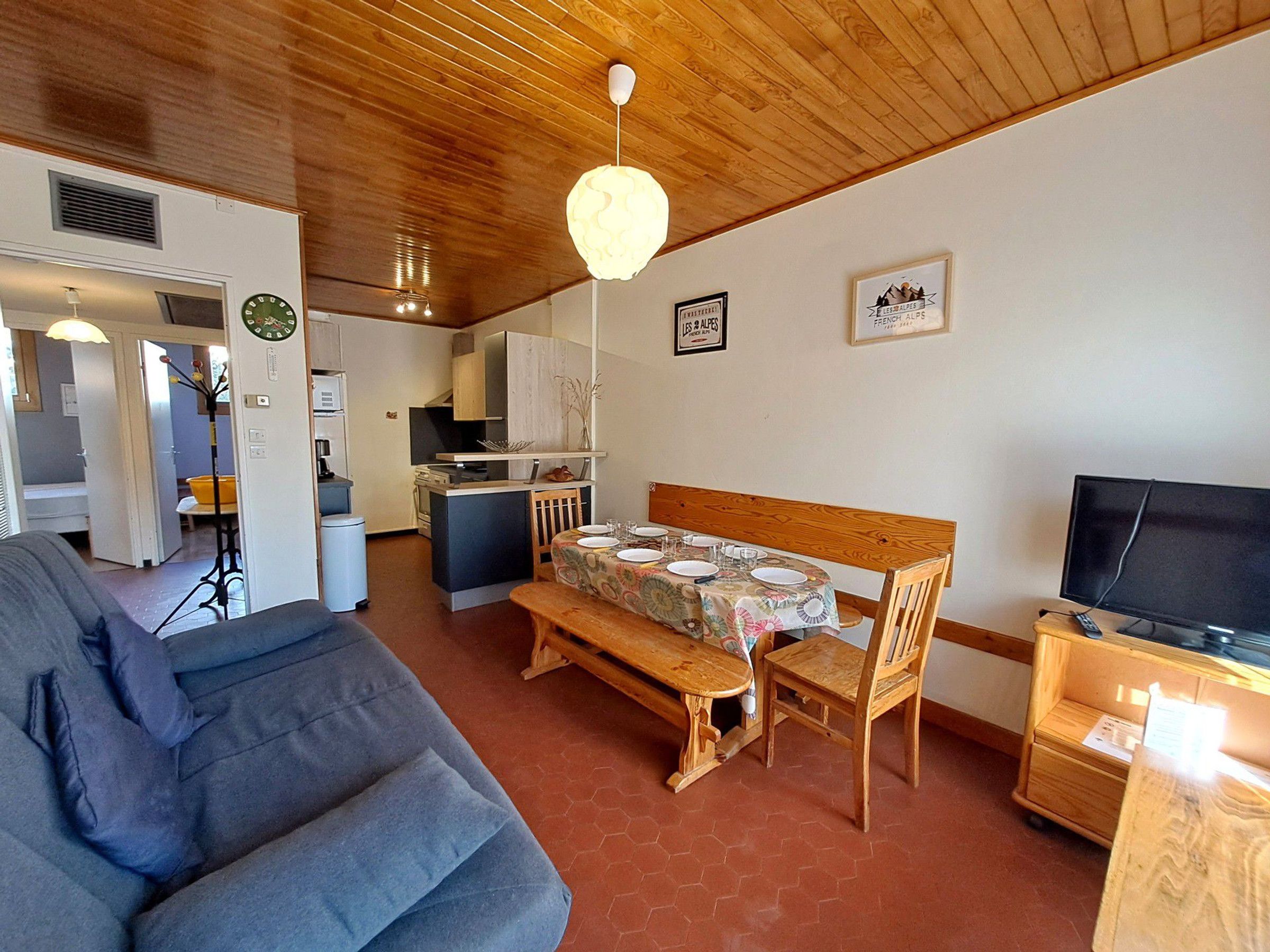 A compact living space with a sofa, a dining table set for two, a television, and a kitchenette.