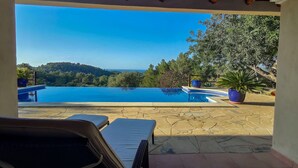 Ein Pool mit Blick auf Meer und Hügel, umgeben von Kübelpflanzen und einer Lounge-Ecke.
