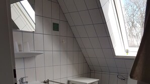 Ett litet, modernt badrum med ett takfönster, vita kakelplattor, ett handfat, en toalett och ett vitt förvaringsskåp.