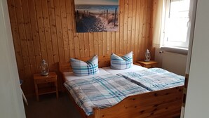 Ett sovrum med träpanel på väggarna, en säng, två sängbord, en tavla som hänger på väggen och ett fönster.