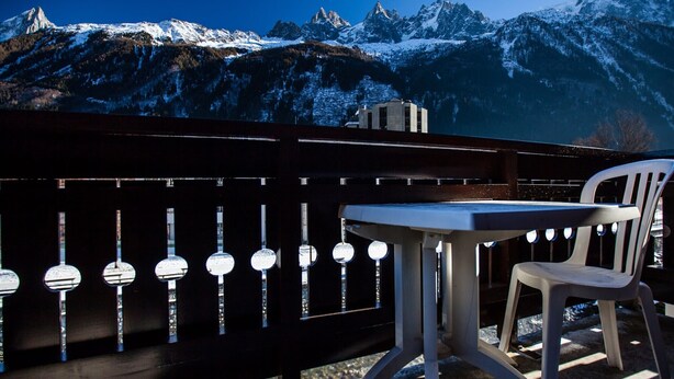 Ein Balkon mit Tisch und Stuhl, mit Blick auf schneebedeckte Berge.