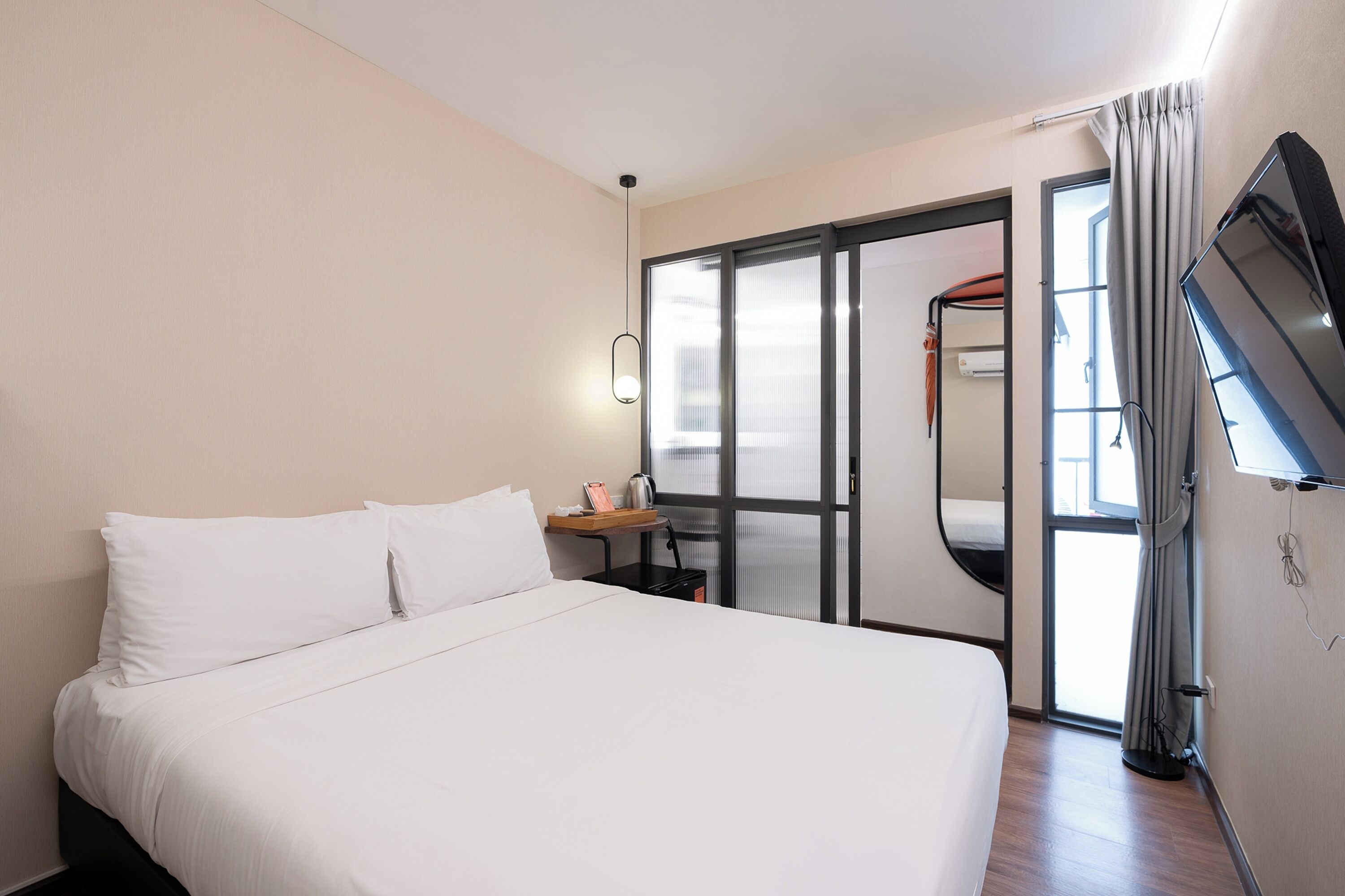 A hotel room with a bed, a desk, a mirror, and a sliding door leading to a balcony.