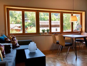 Une pièce avec une grande fenêtre, une table à manger, des chaises, un canapé et une lampe.