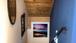 A staircase with a wooden ceiling, a blue wall, and a framed picture of a sunset. - Apartment "Am Berg" in Fischbachau, Birkenstein (Fischbachau)