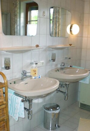 A bathroom with two sinks, a mirror, and a trash can.