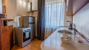 Una kitchenette compacta con estufa, horno, refrigerador y un lavamanos con tetera.