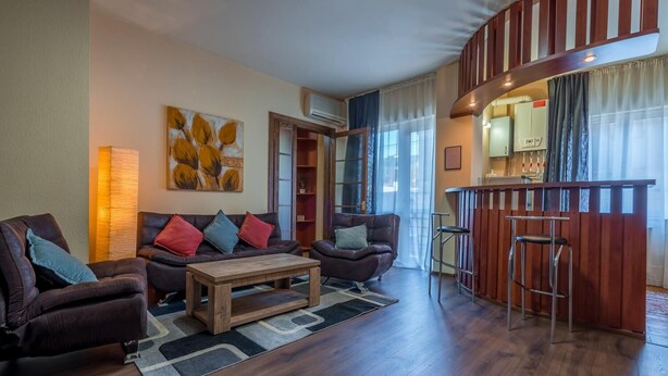 Una sala de estar moderna con un conjunto de sofás, una mesa de centro y una zona de bar con taburetes.