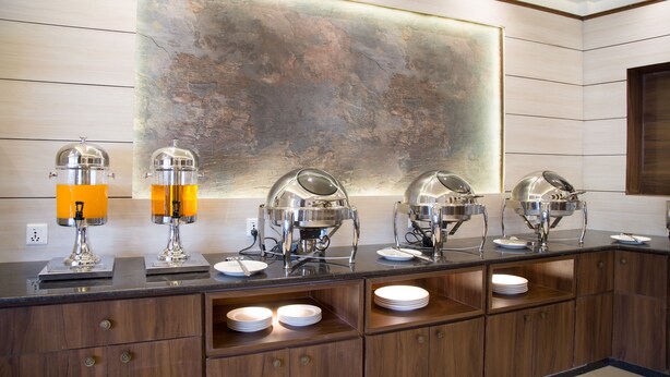 Een buffetopstelling met meerdere zelfbedieningspunten, waaronder dispensers voor warme en koude dranken, en een grote abstracte muurschildering op de achtergrond.