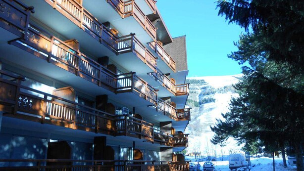 Ein mehrstöckiges Hotel mit Balkonen, einer schneebedeckten Zufahrt und einer gebirgigen Kulisse.