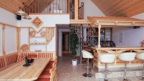 A spacious dining area with a wooden table and chairs, a bar with stools, and a staircase leading to an upper level. - Tischlmuehle Appartements & mehr (Mitterberg-Sankt Martin)