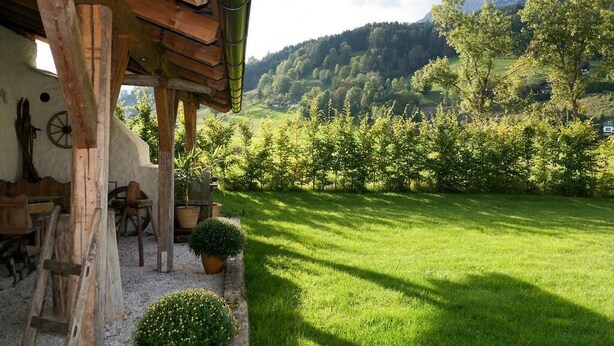 A rustic wooden building with a stone wall, a wooden table, and chairs outside. - Tischlmuehle Appartements & mehr (Mitterberg-Sankt Martin)