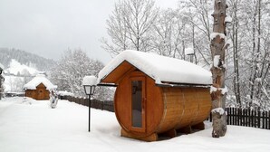 A wooden cabin with a snow-covered roof, surrounded by a wooden fence and snow-covered trees. - Tischlmuehle Appartements & mehr (Mitterberg-Sankt Martin)