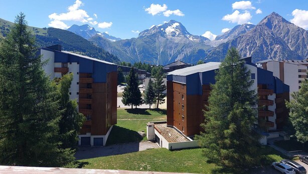 A modern building complex with multiple floors, surrounded by lush greenery and a mountainous backdrop.