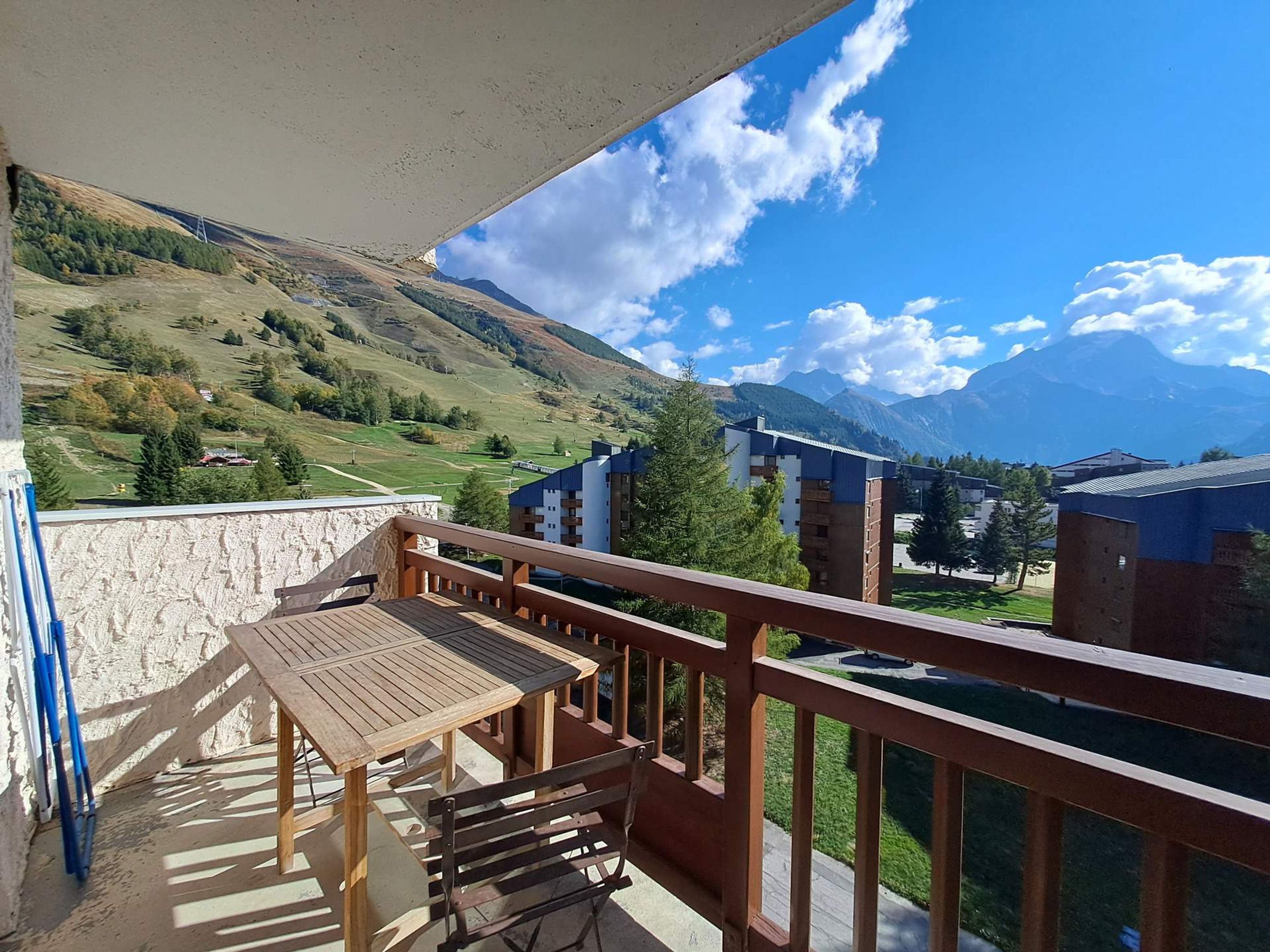 A balcony with a wooden table and benches, overlooking a mountainous landscape with buildings in the background.