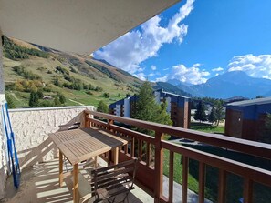 A balcony with a wooden table and benches, overlooking a mountainous landscape with buildings in the background. - Cozy studio at the foot of the slopes, for 4 people, mountain view (Les Deux Alpes)