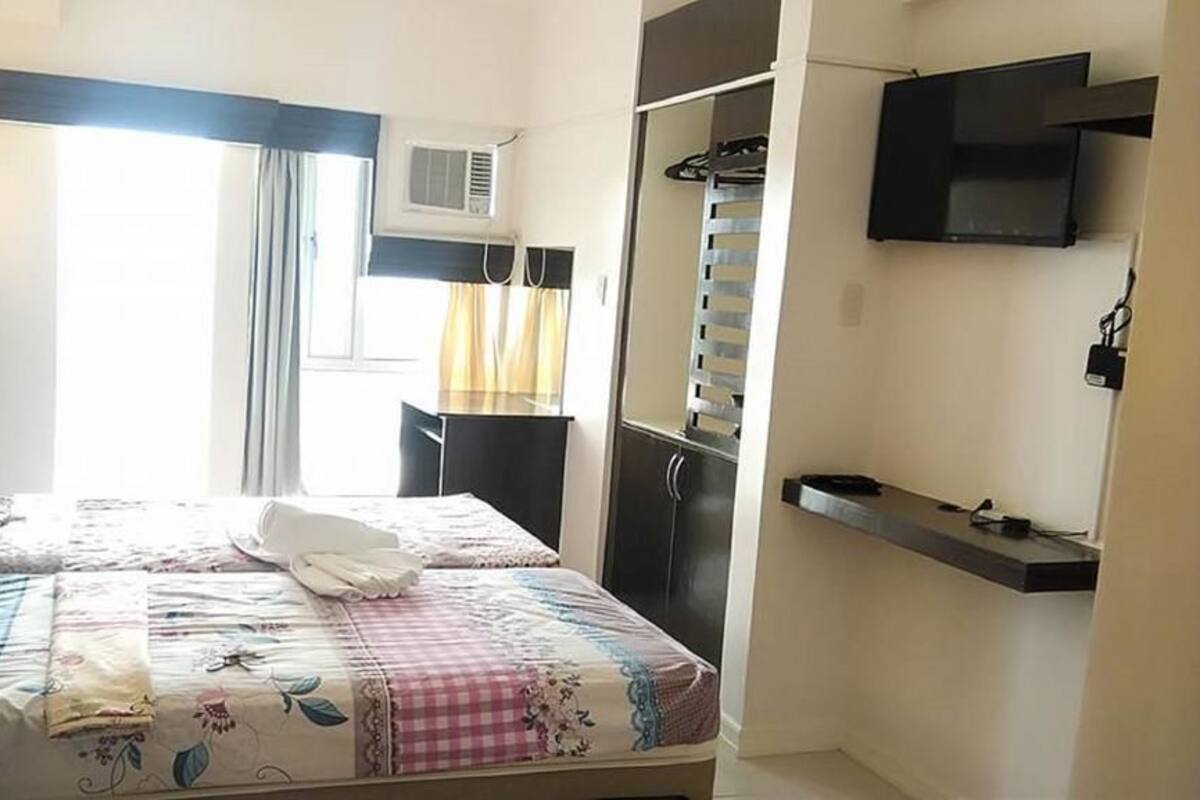 Quarto com cama, escrivaninha, televisão e guarda-roupa.