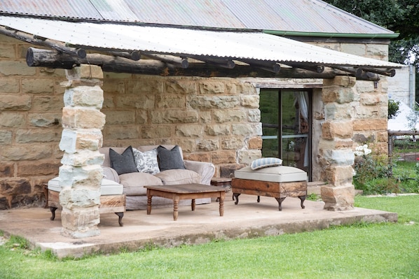 A stone building with a covered patio, stone pillars, a sofa, a coffee table, and a cushioned bench.