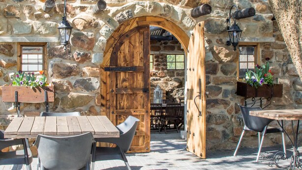 An outdoor stone wall with a wooden door, a table with chairs, and hanging lanterns. - Flitwick Ranch (Greater Kokstad)
