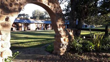 Un arco de piedra que da paso a un edificio con tejado azul, rodeado de césped y árboles.