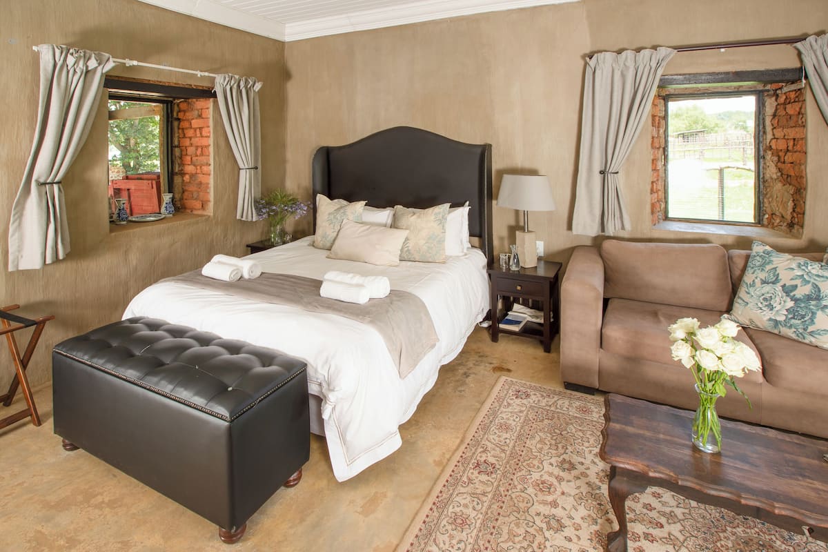 A bedroom with a large bed, a sofa, a coffee table, and a window with curtains.