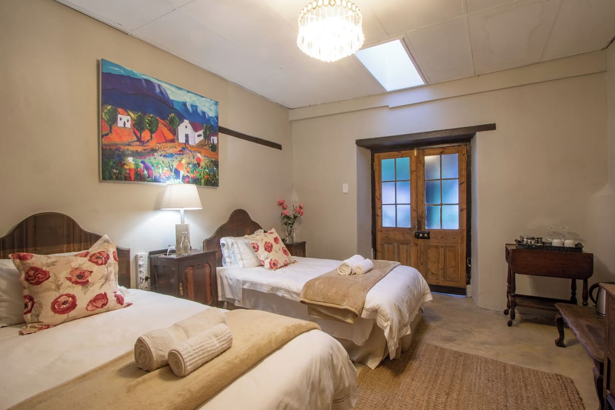 A hotel room with two beds, a wooden door, a chandelier, and a painting on the wall.
