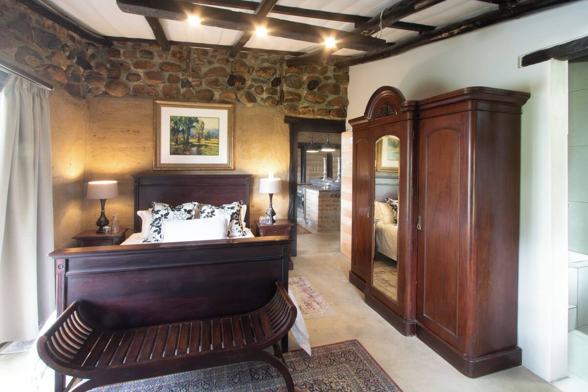 A bedroom with a wooden bed, a bench, a wardrobe, and a stone wall.
