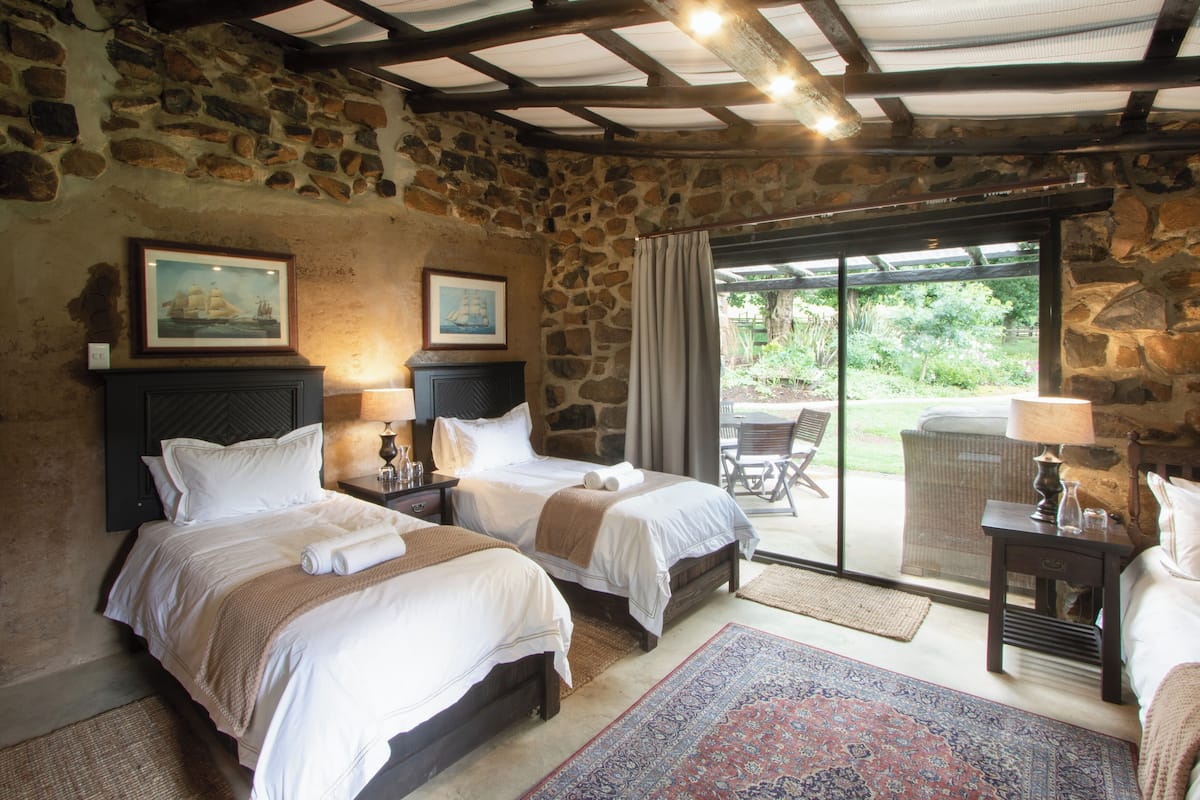 A room with two beds, stone walls, and a view of the outdoors.