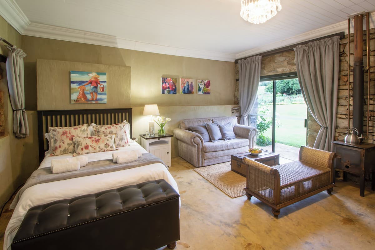 A bedroom with a large bed, a sofa, a wicker chair, and a stone fireplace.