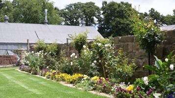 A garden with a stone wall, a metal roof, and a variety of colorful flowers.