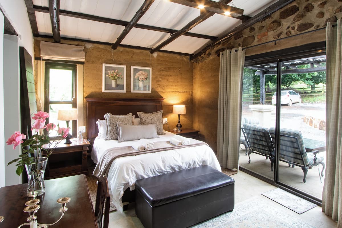 A bedroom with a large bed, bedside tables, a nightstand, a bench, and a view of the outside.