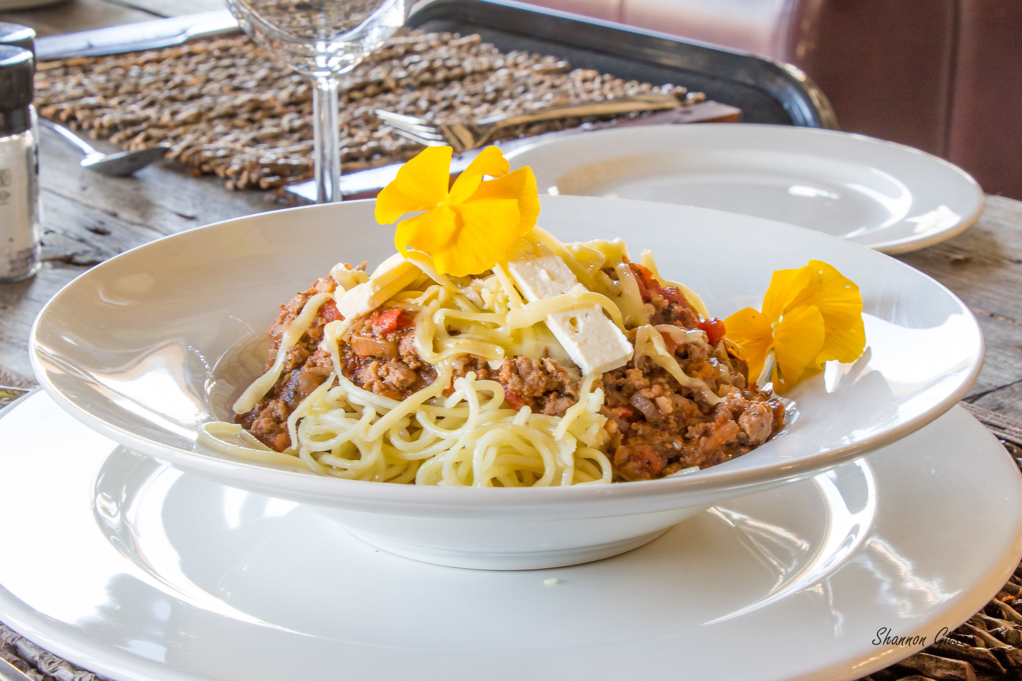 Un plato de espagueti con salsa de carne y una flor amarilla como adorno.