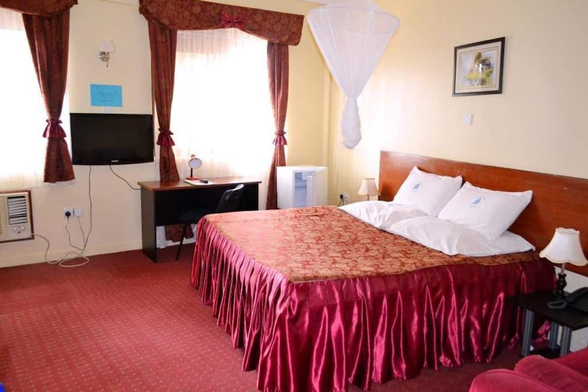 Ett hotellrum med en säng, ett skrivbord, en tv och ett myggnät.