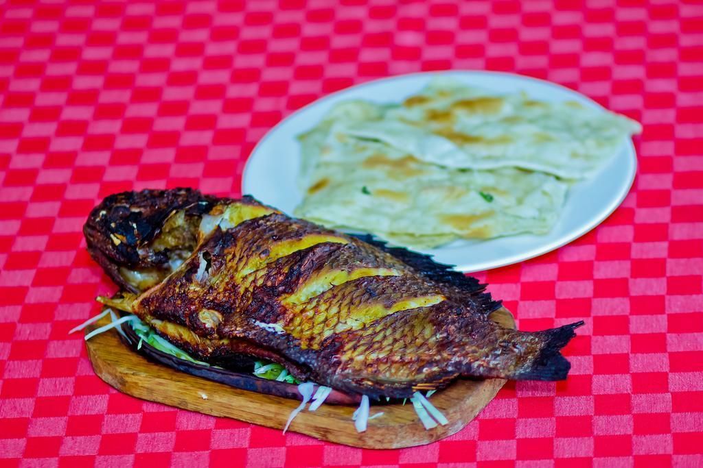A grilled fish on a wooden board with a plate of flatbreads in the background.