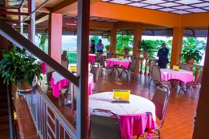 Un restaurante al aire libre con mesas cubiertas de manteles rosas, un letrero de 'No Fumar' y plantas en macetas.