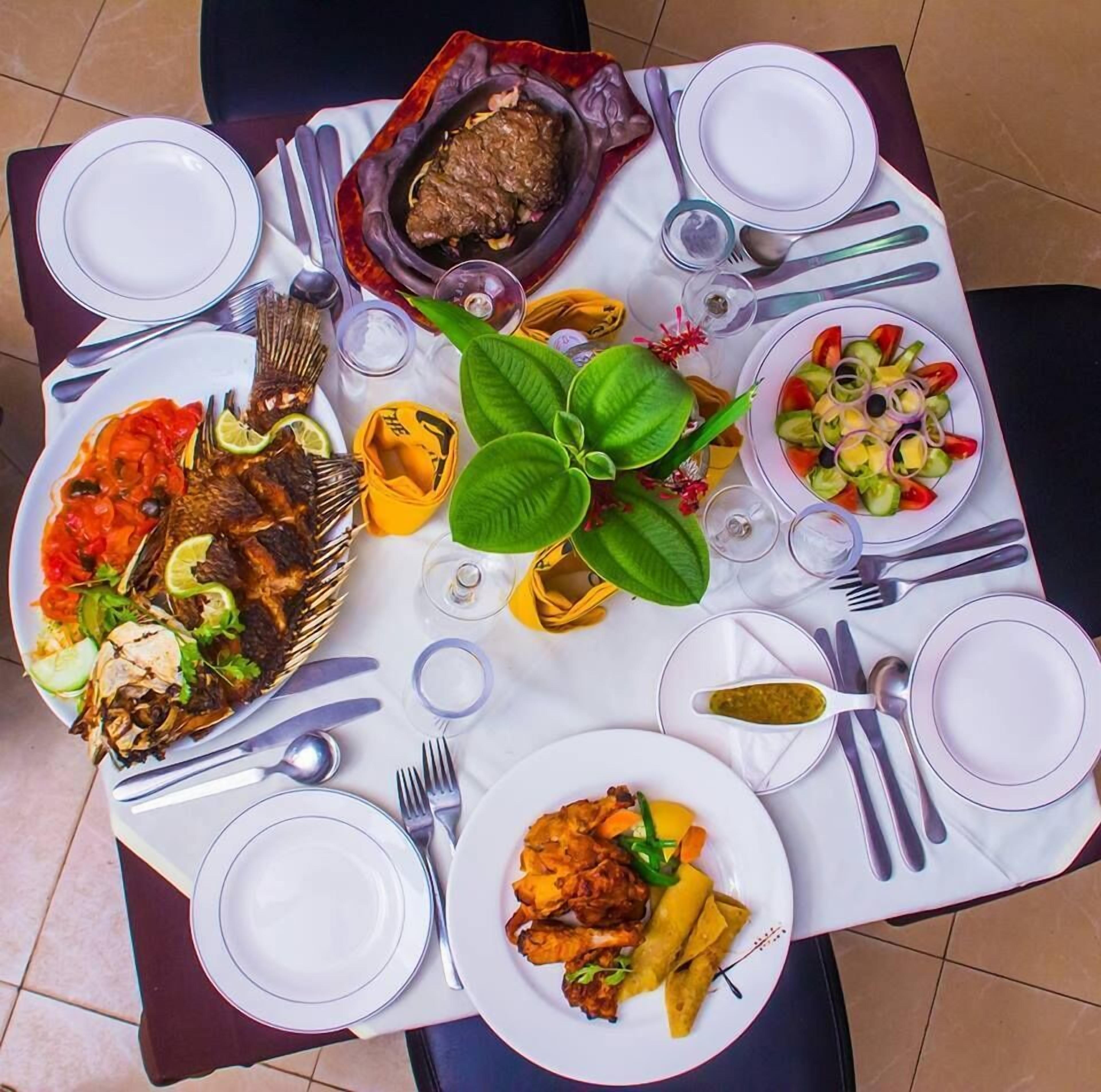A dining table with various dishes, including grilled fish, a salad, and a meat dish, along with cutlery and glasses.