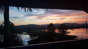 Vista al atardecer desde una ventana con vista a un cuerpo de agua, un puente y colinas distantes.