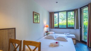 Una camera d'albergo con un letto, una scrivania con sedie, una lampada e una finestra con tende.