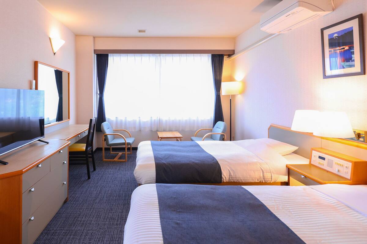 Ein Hotelzimmer mit Bett, Schreibtisch, Stuhl, Fernseher und einem fensterbepflanzten Fenster.