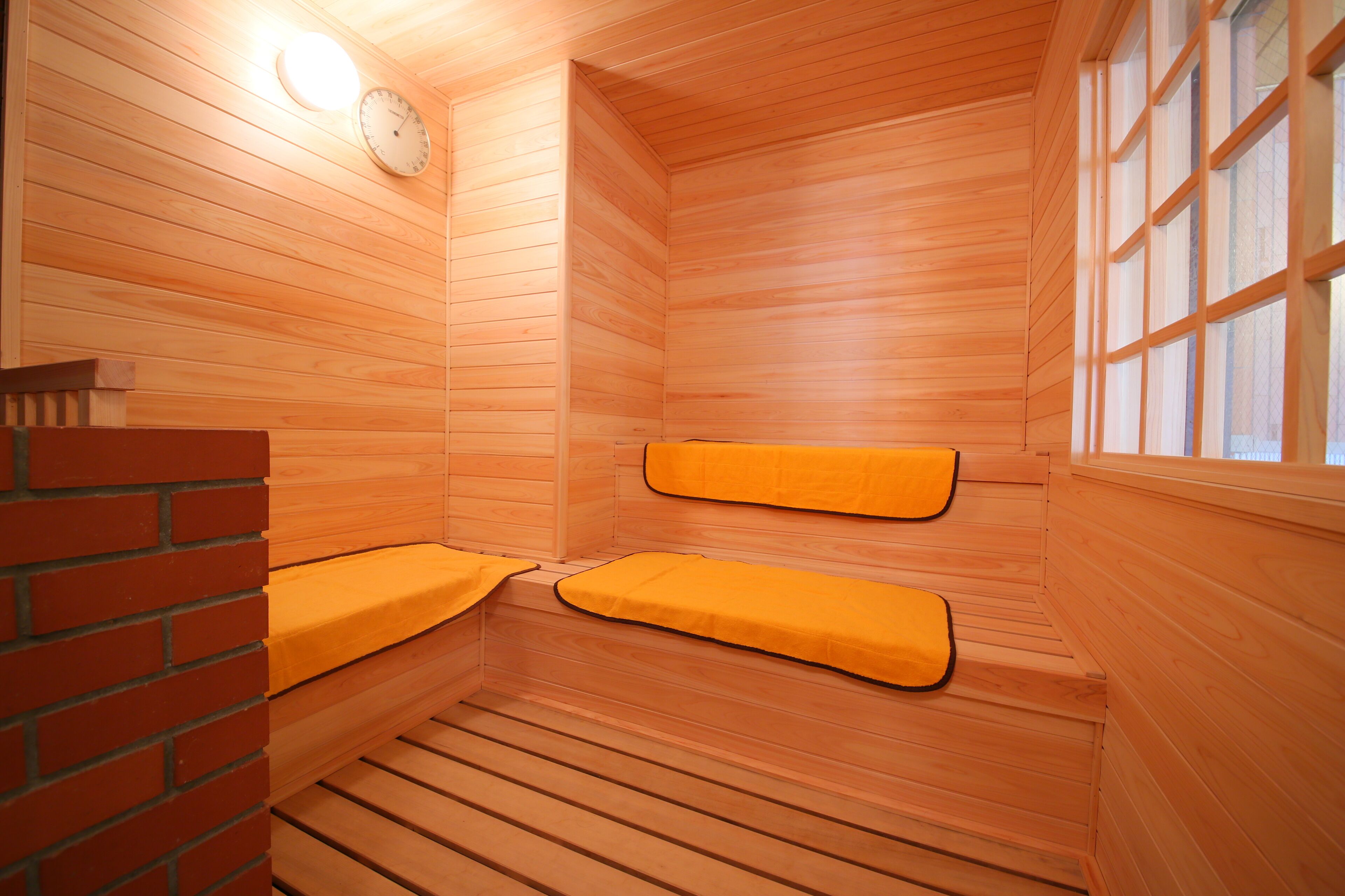 Un sauna aux murs en bois, avec une horloge et deux bancs dotés de coussins jaunes.