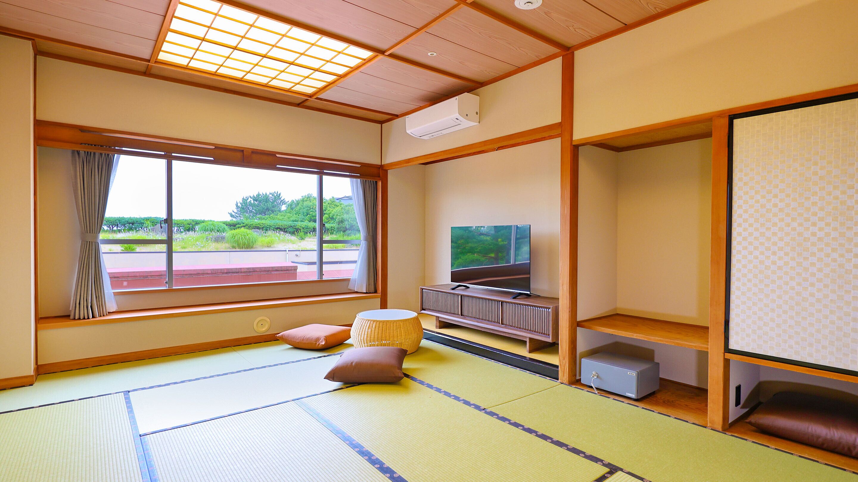A traditional Japanese room with tatami flooring, a television, a heater, and a view of greenery outside.