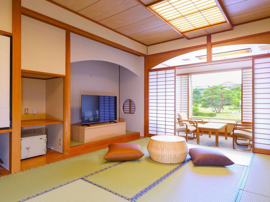 Una habitación japonesa tradicional con suelo de tatami, un televisor y vistas a un jardín.