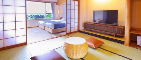 A traditional Japanese-style room with tatami flooring, a bed with a blue blanket, a television on a wooden stand, and a view of a garden through a sliding door.