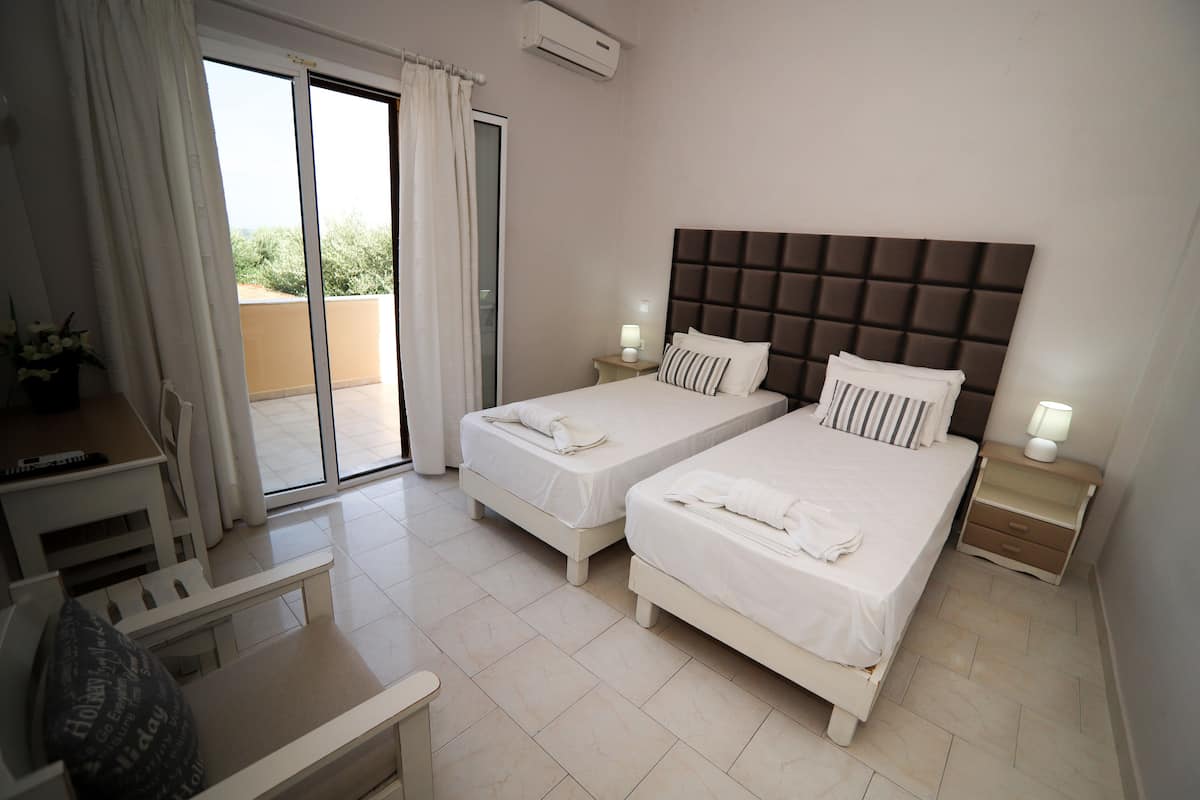 Habitación de hotel con dos camas, un escritorio, una silla y un balcón con vistas.