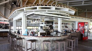 A bar area with a stone counter, multiple stools, and a variety of bottles and glasses. - Scheria Hotel (Corfu)