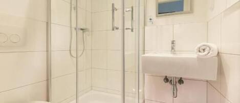 Un baño moderno con ducha de vidrio, un lavabo blanco y un inodoro.