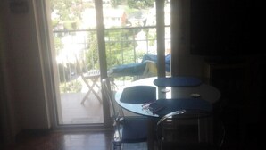 A room with a large window, a table with a chair, and a view of a garden and buildings outside. - Studio apartment 10 minutes from the 5 Terre (Moneglia)
