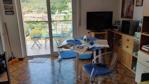 A room with a balcony, a TV, a table with papers, and a bookshelf. - Studio apartment 10 minutes from the 5 Terre (Moneglia)